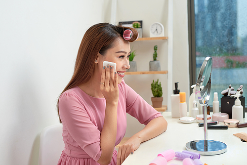 Cosmetic beauty procedures and makeover concept. Woman in hair curlers beautiful young woman using cotton pads at home