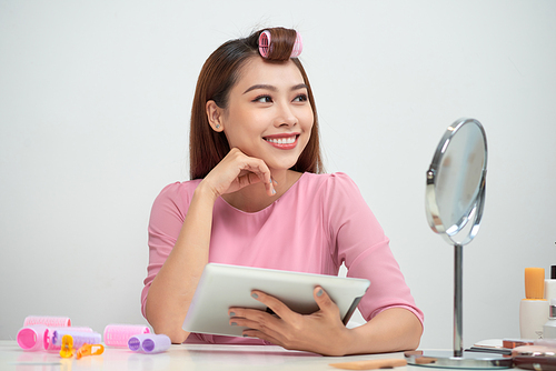 Thoughtful pretty woman wearing hair curlers using tablet pc sitting in living room