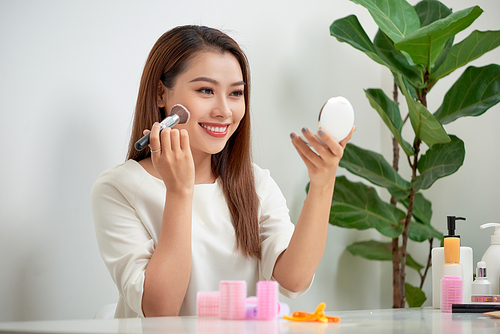 young beautiful woman applying her make-up with a big brush , looking in a mirror