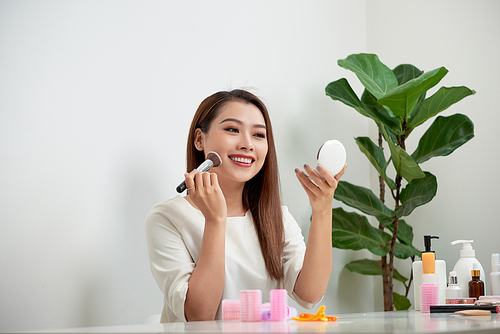 young beautiful woman applying her make-up with a big brush , looking in a mirror