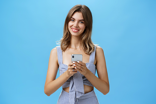 Friendly pleasant good-looking woman in matching outfit holding smartphone over chest tilting head smiling broadly showing cute gapped teeth being delighted after reading heartwarming message. Lifestyle.