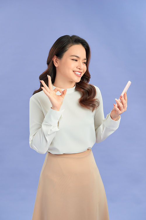 Young woman talking mobile over isolated purple background showing ok sign with fingers