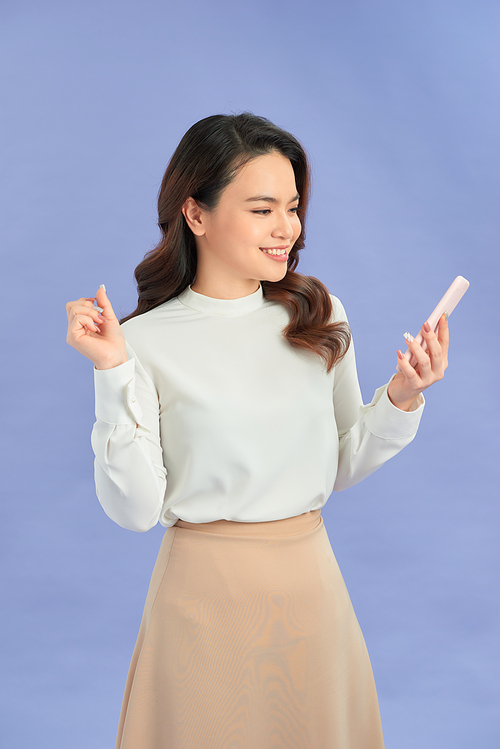 Portrait of a smiling casual woman holding smartphone over purple background