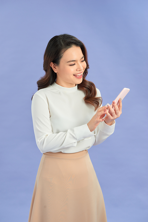 Photo of cheerful businesswoman smiling and using cellphone isolated over purple background