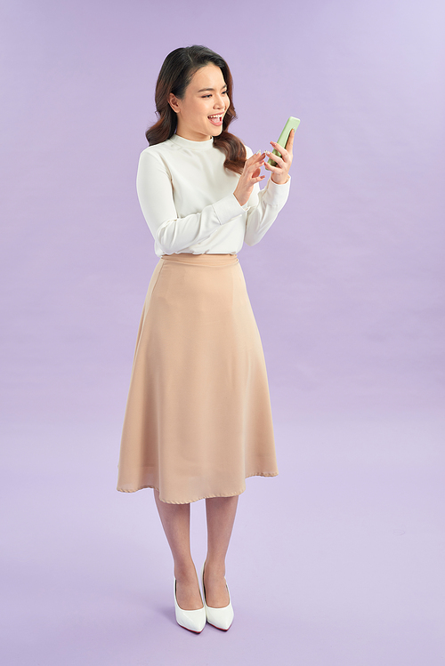 Portrait of a cheerful girl looking at mobile phone isolated over purple background