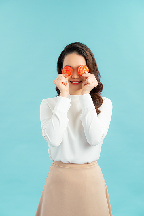 Healthy young Asian woman holding fresh tomato slice over blue isolated background. Healthy and beauty skin care concept.