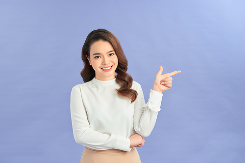Young woman pointing at blank copy space, isolated over purple