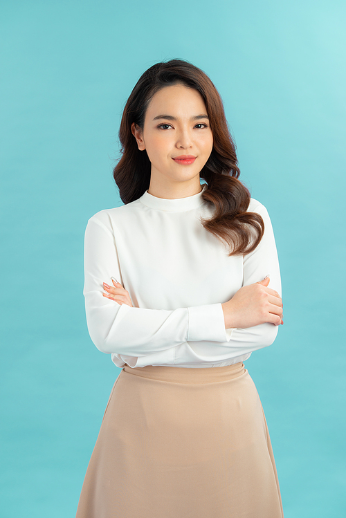 Portrait of a happy confident woman standing with arms folded and looking at camera isolated over blue background