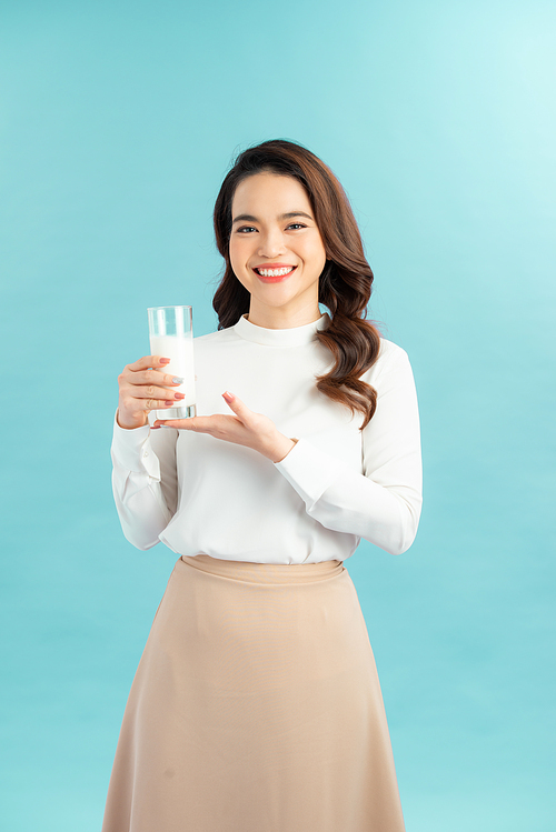 Portrait of a happy Asian woman drinking a glass of milk. Standing in front of a blue wall.