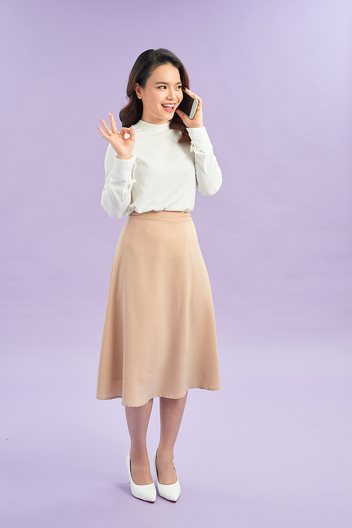 Happy woman talking on the phone and showing ok sign isolated on a purple background