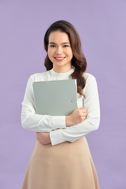 Happy beautiful young business woman standing and holding clipboard over purple background
