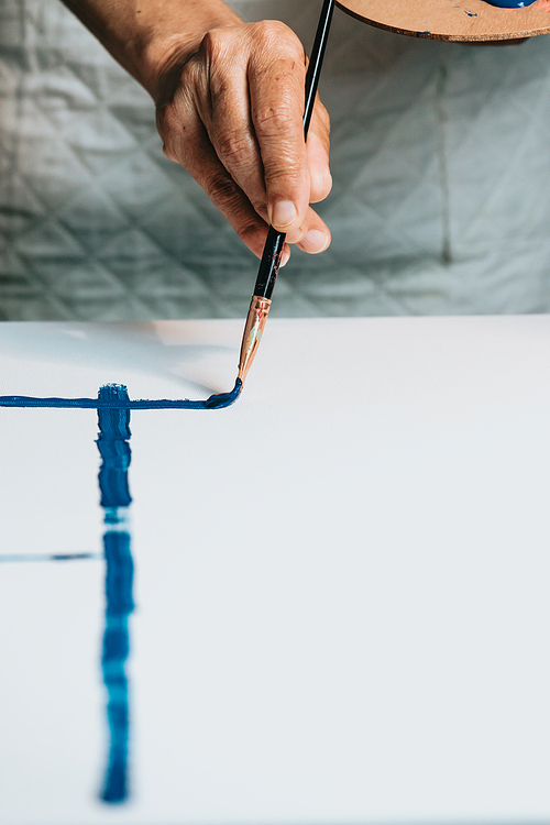 Close-up of Female senior old Artist Hand, Holding Paint Brush and Drawing Painting with blue Paint. Colorful, Emotional Oil Painting. Contemporary Painter Creating Modern Abstract Piece of Fine Art