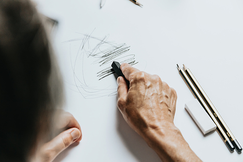 High angle view of a senior Caucasian woman drawing sketches in studio. Creativity, education and people concept,cognitive functions clock drawing self assessment test at home with positive results