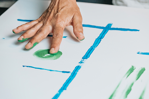 Close-up of Female senior old Artist Hand, Holding Paint Brush and Drawing Painting with blue Paint. Colorful, Emotional Oil Painting. Contemporary Painter Creating Modern Abstract Piece of Fine Art