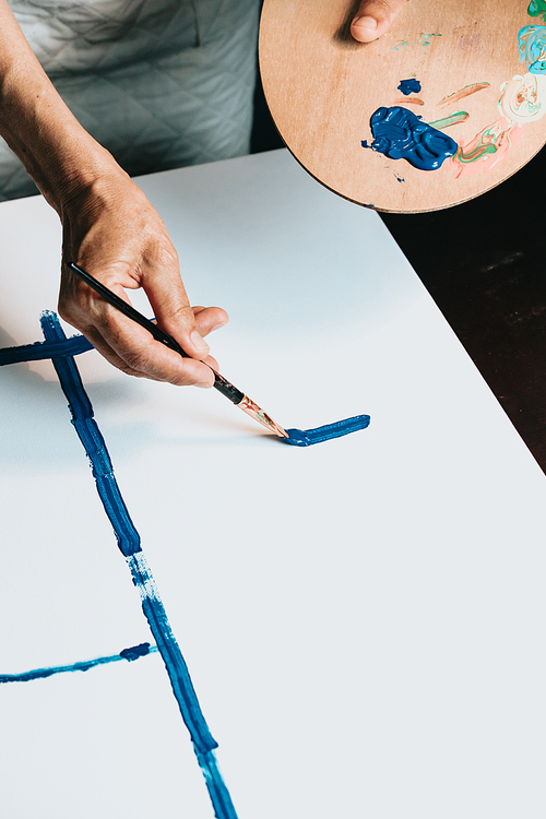 Close-up of Female senior old Artist Hand, Holding Paint Brush and Drawing Painting with blue Paint. Colorful, Emotional Oil Painting. Contemporary Painter Creating Modern Abstract Piece of Fine Art