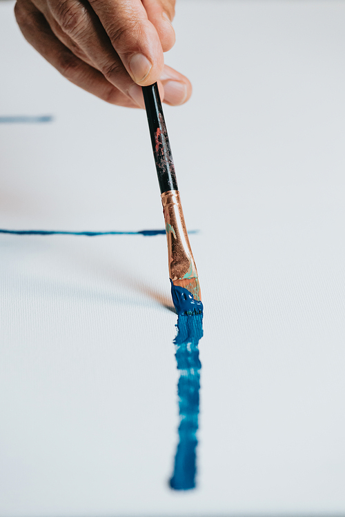 Close-up of Female senior old Artist Hand, Holding Paint Brush and Drawing Painting with blue Paint. Colorful, Emotional Oil Painting. Contemporary Painter Creating Modern Abstract Piece of Fine Art