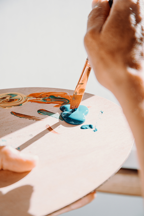 Close-up of Female senior old Artist Hand, Holding Paint Brush and Drawing Painting with blue Paint. Colorful, Emotional Oil Painting. Contemporary Painter Creating Modern Abstract Piece of Fine Art