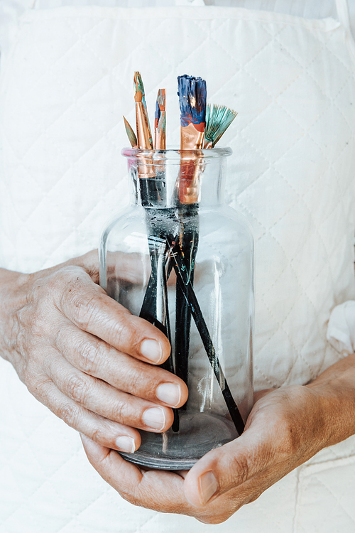 Old hands grabbing a bottle filled with paint pencils and brushes, ready for painting acrylic. Artistic concepts, artist concept.