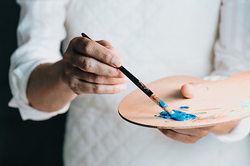 Studio image of an old woman painting a canvas with blue paint. Artist studio concept. Old artist