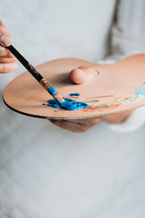 Close-up of Female senior old Artist Hand, Holding Paint Brush and Drawing Painting with blue Paint. Colorful, Emotional Oil Painting. Contemporary Painter Creating Modern Abstract Piece of Fine Art