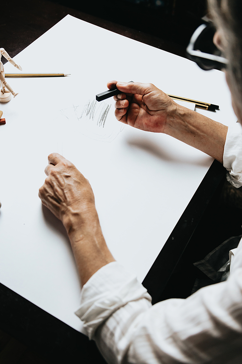 High angle view of a senior Caucasian woman drawing sketches in studio. Creativity, education and people concept,cognitive functions clock drawing self assessment test at home with positive results