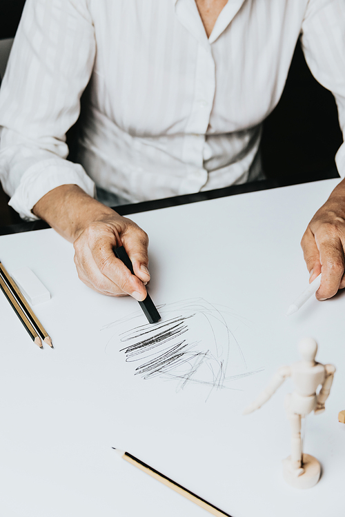 High angle view of a senior Caucasian woman drawing sketches in studio. Creativity, education and people concept,cognitive functions clock drawing self assessment test at home with positive results