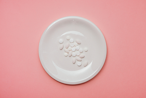 Pills served as a healthy meal. Drug capsule on white plate on pink background