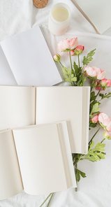 Blank opened books and flowers on white bed, flat lay, mock up, flat lay
