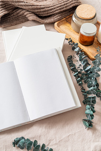Blank opened book, candles and eucalyptus leaves on white bed, flat lay, mock up, flat lay