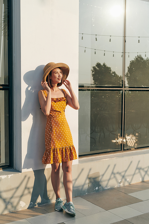 Summer sunny lifestyle fashion portrait of young Asia woman wearing hat and yellow dress
