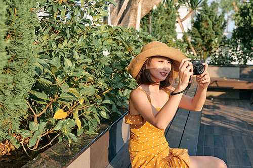 Fashionably dressed woman sitting in the park and using camera