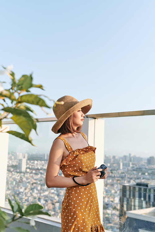 Young Asian girl standing on roof top and using camera to take picture. Summer concept.