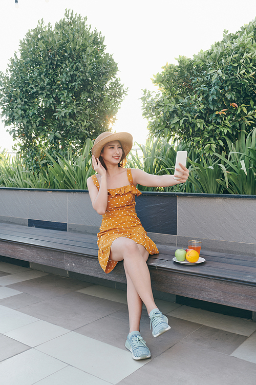 Young Asian girl using smartphone to selfie and siting at park