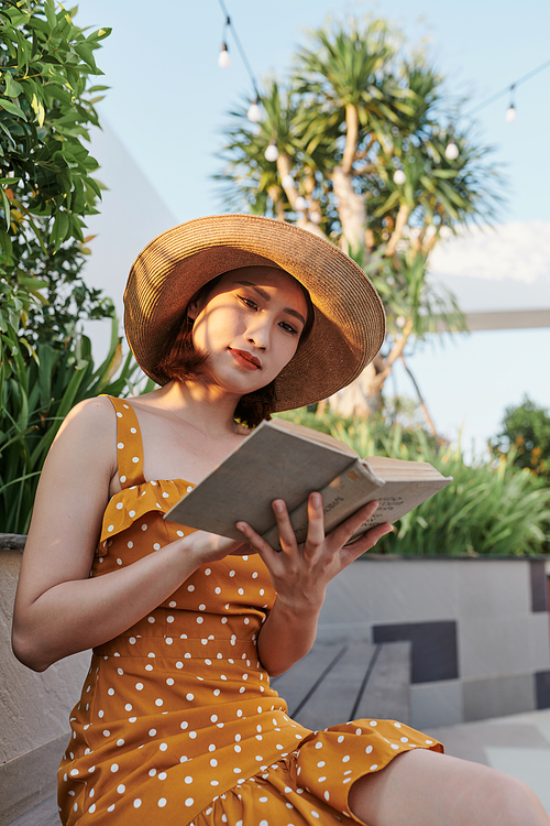 Asian young woman sitting behind a tree reading a book in the park