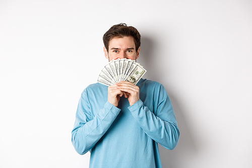 Cheerful shopper holding money for shopping, standing with dollars and smiling, standing over white background in casual clothes.