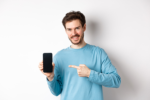 E-commerce and shopping concept. Smiling caucasian man pointing finger at empty smartphone screen, showing online offer, white background.