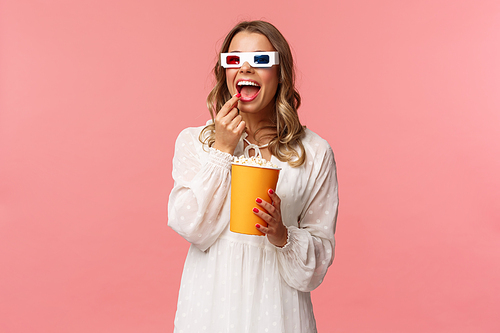 Leisure, going-out and spring concept. Portrait of attractive young woman in white dress enjoying watching interesting movie on full screen at cinema, eating popcorn and wearing 3d glasses.