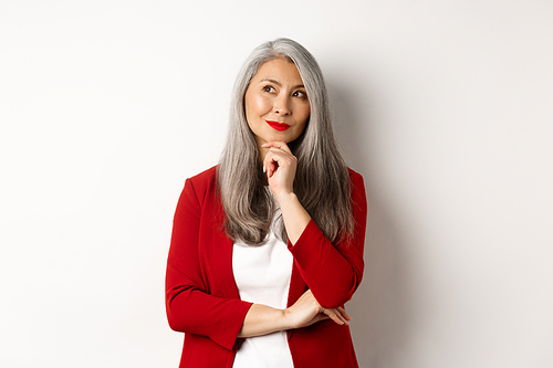 Business concept. Smiling mature lady in red blazer, smiling and looking satisfied while thinking, standing over white background.
