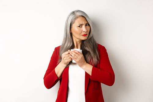 Business people concept. Greedy asian businesswoman protecting her coffee and frowning at camera, standing over white background.