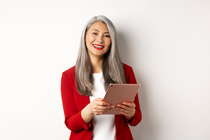Business. Successful senior businesswoman working with digital tablet and smiling, standing in red blazer over white background.
