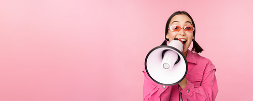 Attention, announcement concept. Enthusiastic asian girl shouting in megaphone, advertising with speaker, recruiting, standing over pink background.