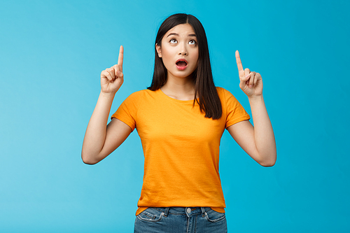 Surprised impressed asian girl dark short hairstyle drop jaw, gasping amazed look pointing up astonished, check out incredible offer, express full disbelief and amazement, stand blue background.