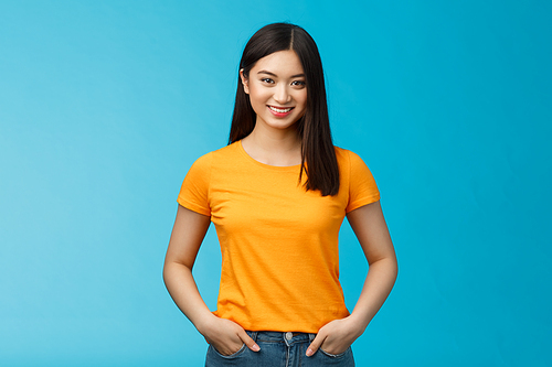 Confident assertive smiling asian woman stand blue background look camera, hold hands jeans pockets express self-assured vibe, enjoy seeing positive results skincare procedures, wear yellow t-shirt.