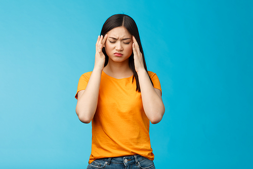 Distressed tired asian woman dark haircut cringe touch temples, suffer huge migraine need painkillers, painful headache, feel dizzy, stand blue background intense drained. Copy space