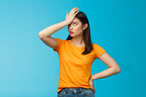 Annoyed arrogant asian girl punch forehead make facepalm sign, roll eyelids irritated pissed, cannot stand lame talks look disappointed ingorant, unwilling to listen, stand blue background.