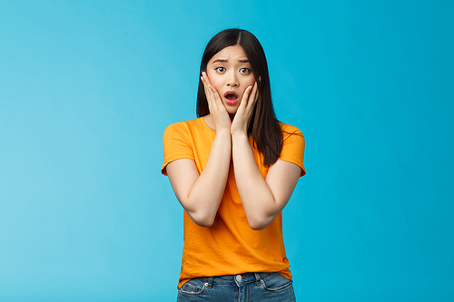 Shocked concerned young asian girl look empathy camera, gasping open mouth worried, frowning upset hear frustrating news, pitty feel sorry for friend, touch cheeks speechless, stand blue background.