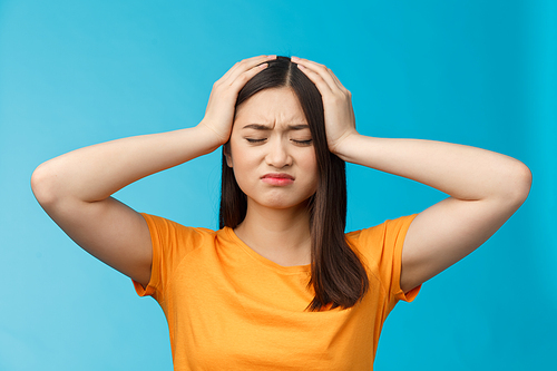 Close-up perplexed upset cute asian girl tired, exhausted piled up work, whining complain tough day, grab head troubled, distressed, close eyes grimacing bothered, stand blue background.