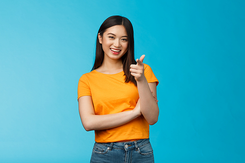 Hey you got point. Cheerful cute asian lively girl dark short haircut pointing camera finger-pistol smiling broadly, encourage friend make move, congratulate coworker good job, stand blue background.