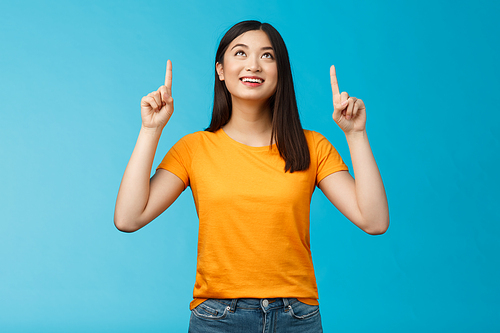 Asian girl contemplating view enjoy summer vacation like sunny days, look pointing up amused, feel enthusiastic upbeat, smiling broadly showing top promo, gaze with interest, blue background.