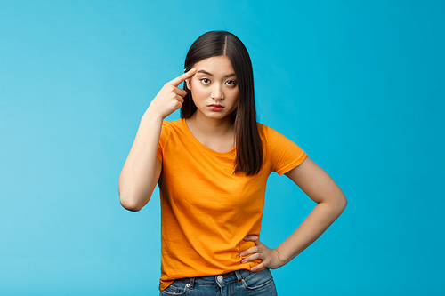 Pissed irritated asian girl look annoyed bend camera roll finger on temple stare camera bothered dismay, asking are you out mind, show person crazy weird, stand blue background. Copy space